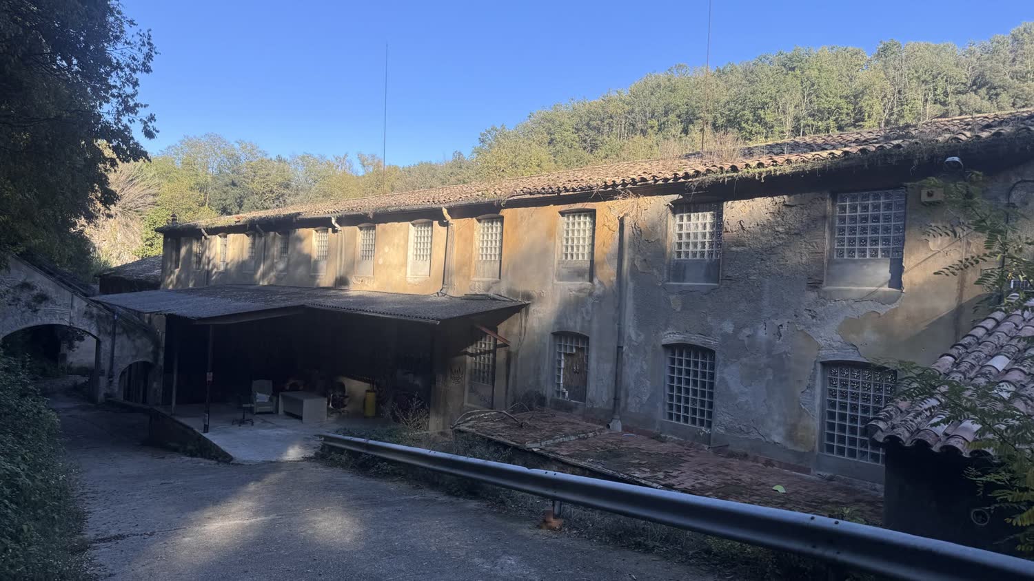 L&rsquo;edifici de la fàbrica de 1886, de pedra i arrebossat, amb el bosc al darrere
