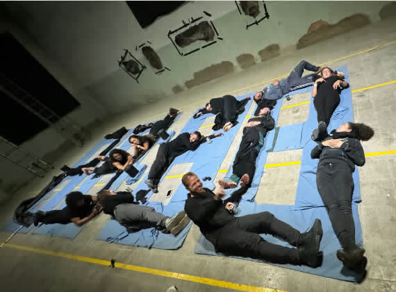 Un grup de persones estirades sobre màrfegues blaves a la nau de la fàbrica durant una performance